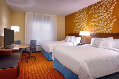 A hotel room with two beds, a desk, a TV, and decorative wall accents. Bright and modern decor with natural light.