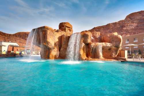 A scenic pool with waterfalls cascading over rock formations, surrounded by lounge chairs and a clear blue sky.