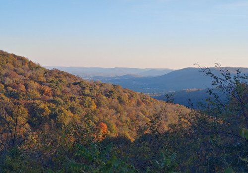 A scenic view of rolling hills covered in autumn foliage under a clear blue sky.