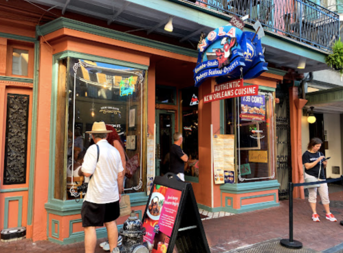 A colorful restaurant entrance with a sign for authentic New Orleans cuisine, featuring people outside and a menu display.