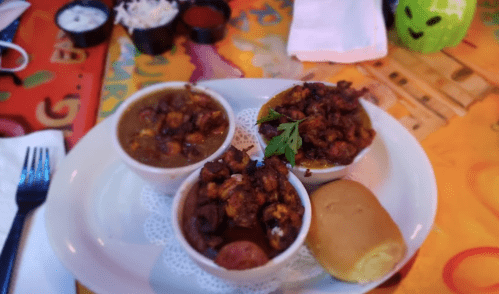 Three bowls of spicy seafood stew with a roll, served on a colorful table.