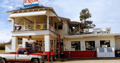 A vintage gas station with a convenience store, featuring an Exxon sign and a red pickup truck parked outside.