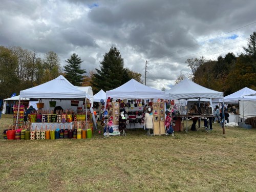 A vibrant outdoor market with white tents displaying colorful crafts and goods under a cloudy sky.