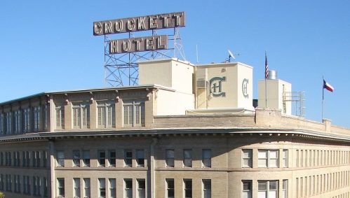 Historic Crockett Hotel building with a rooftop sign, featuring a classic facade and flags in front.