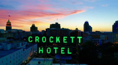 Neon sign for Crockett Hotel against a colorful sunset skyline of a city.