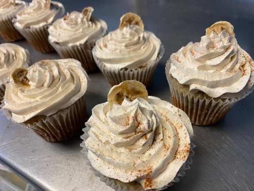 A close-up of cupcakes topped with swirls of cream and a slice of banana, arranged on a silver surface.