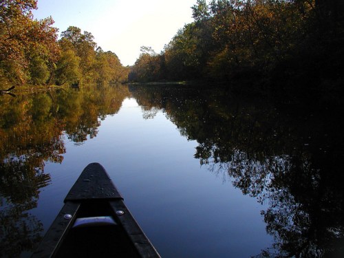Canoe view on a calm river surrounded by autumn foliage and reflections on the water.