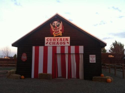 A wooden building with a sign reading "Curtain Chaos," featuring red and white striped curtains and pumpkins outside.