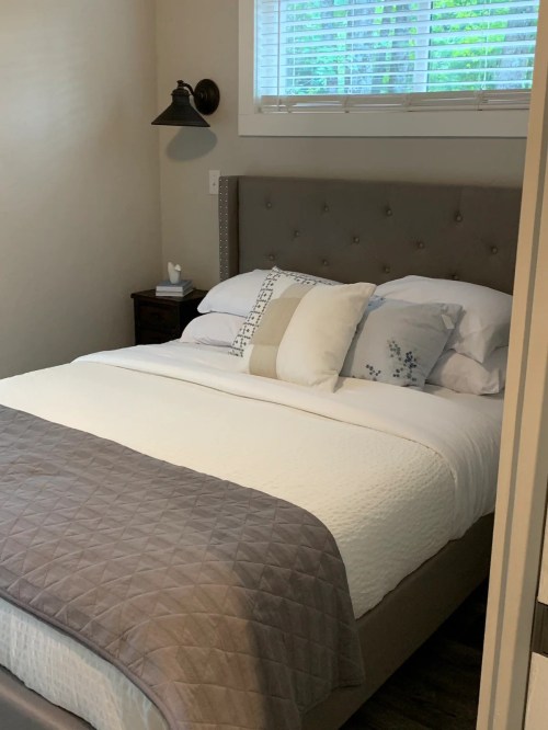 Cozy bedroom featuring a neatly made bed with decorative pillows and a bedside lamp. Natural light from a window.