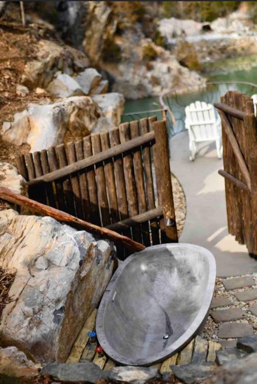 A rustic pathway leads to a serene outdoor area with a stone tub and two white chairs by a tranquil water feature.