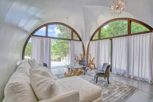 A modern living room with large arched windows, a white sofa, a glass table, and elegant decor.