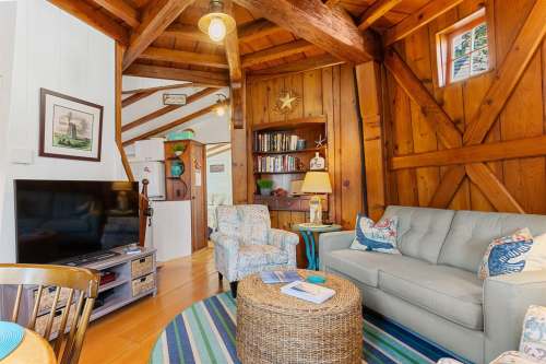 Cozy living room with wooden beams, a gray sofa, a round coffee table, and a TV, featuring warm, inviting decor.