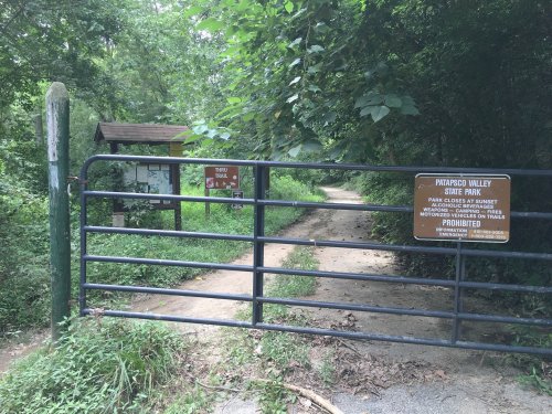 A metal gate at the entrance of Parkwood Valley State Park, surrounded by trees and a dirt path leading into the park.