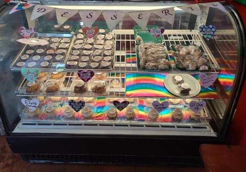 A display case filled with various desserts, including cupcakes and cookies, decorated with colorful banners and labels.