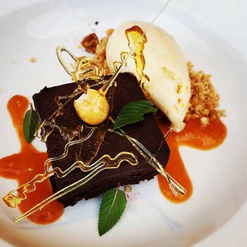 A decadent chocolate dessert with a scoop of ice cream, caramel sauce, and decorative sugar strands on a white plate.
