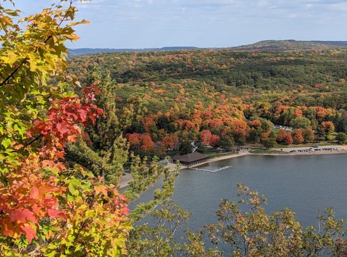 A scenic view of a lake surrounded by vibrant autumn foliage and a beach area, with hills in the background.