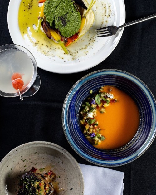 A top-down view of three elegant dishes: a vibrant vegetable stack, a colorful soup, and a gourmet seafood plate.