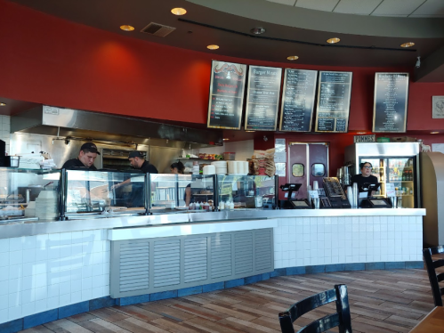 A busy restaurant counter with staff preparing food and a menu displayed on the wall.