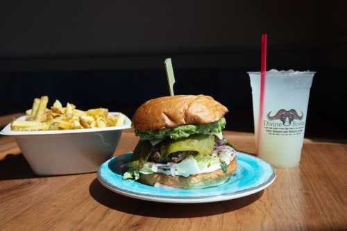 A delicious burger with pickles and avocado, served with fries and a drink on a wooden table.