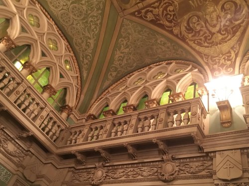 Ornate interior of a historic building featuring intricate ceiling designs and decorative balcony with green windows.