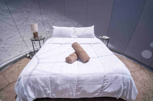 A neatly made bed with white linens and rolled towels, set in a cozy, circular room with soft lighting.