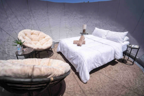 Cozy interior of a tent with a bed, two chairs, and a small table, featuring soft lighting and a relaxed atmosphere.