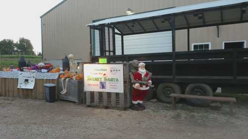 A festive outdoor scene with a Santa figure, pumpkins, and a sign for "Secret Santa" near a trailer.