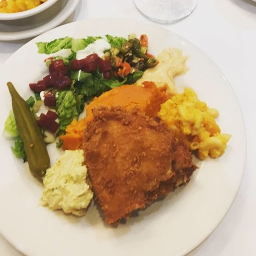 A plate of fried chicken, sweet potatoes, macaroni and cheese, salad, and pickled vegetables.