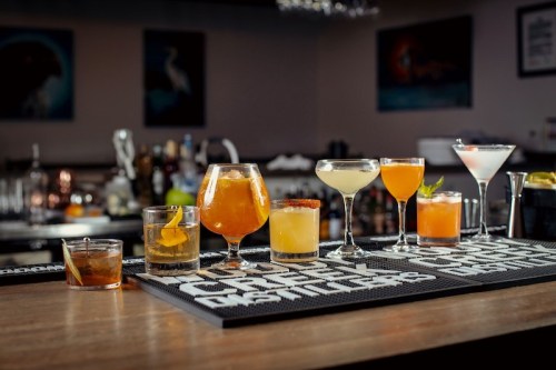 A variety of colorful cocktails displayed on a bar counter, featuring different glasses and garnishes.