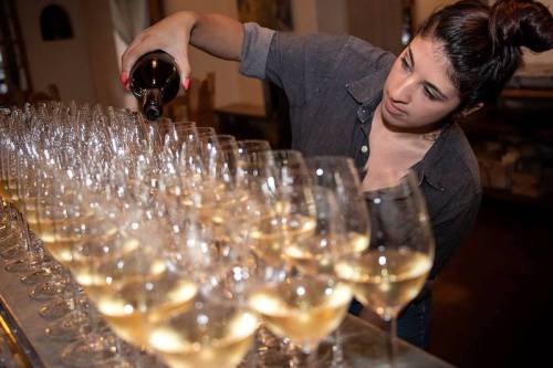 A woman pours wine into a row of sparkling glasses at an event.
