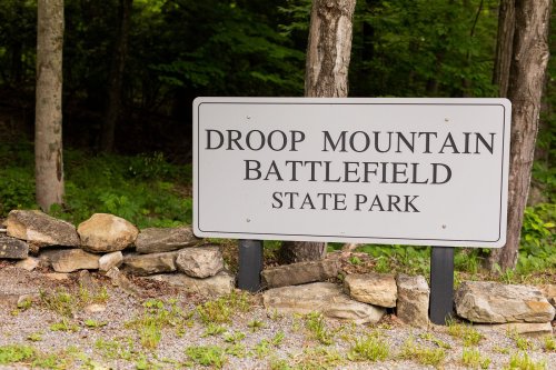 Sign for Droop Mountain Battlefield State Park, surrounded by trees and rocky terrain.