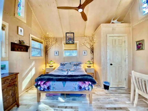 Cozy interior of a small cabin bedroom with a bed, wooden decor, and natural light streaming through windows.