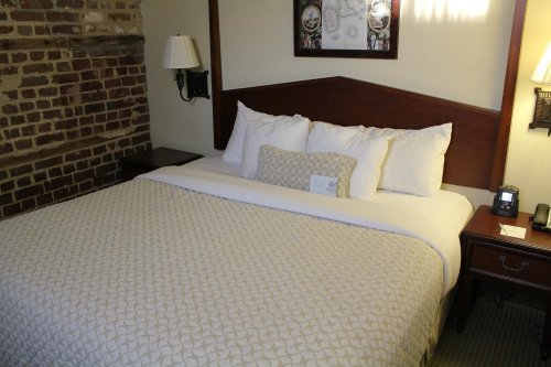 Cozy hotel room featuring a neatly made bed with decorative pillows and a brick wall backdrop.