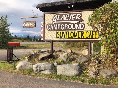 Sign for Glacier Campground and Sunflower Café, with a rustic design and surrounding rocks and greenery.