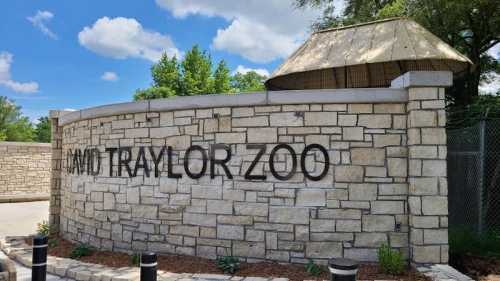 Stone entrance wall of David Traylor Zoo with a thatched roof and blue sky in the background.