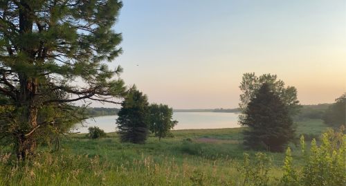 A serene lakeside view at sunset, framed by trees and lush greenery.
