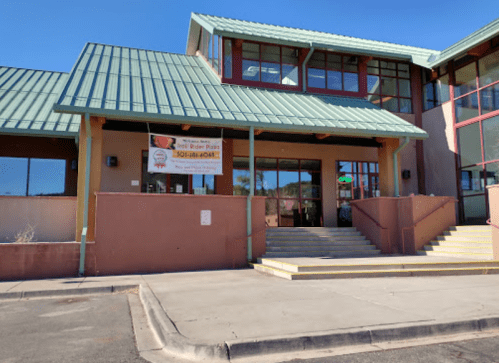 Front view of a building with a green roof, large windows, and steps leading to the entrance, featuring a banner.