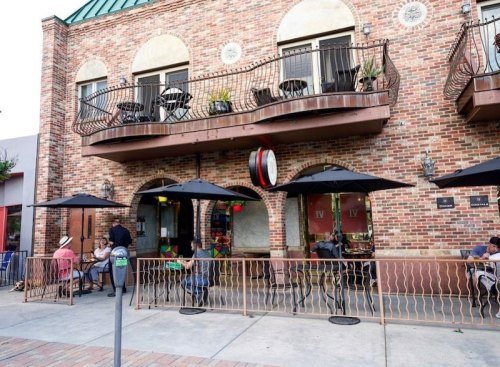 A brick building with outdoor seating, umbrellas, and people dining at a café.