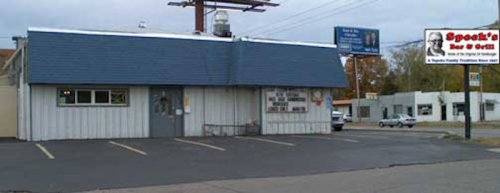A small, single-story building with a metal roof, featuring a sign for "Spooky's Bar & Grill" and a parking lot.