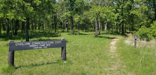 Sign marking the Civilian Conservation Corps original camp site, with a path leading through a wooded area.