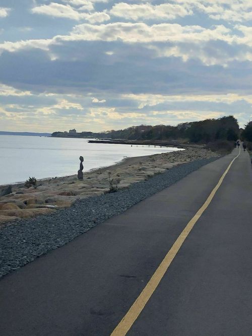 A scenic shoreline with a walking path, rocky beach, and cloudy sky in the background.