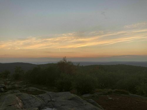 A serene landscape at dusk, featuring rolling hills and a colorful sky with wispy clouds.