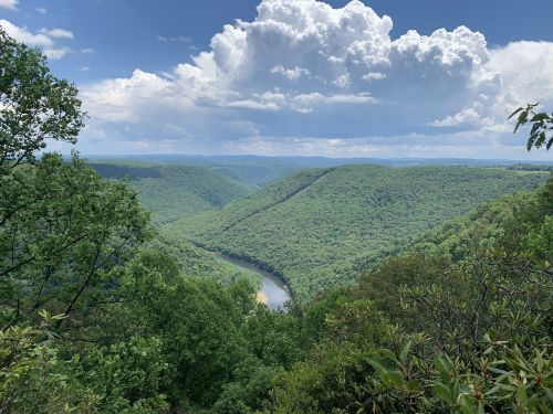 A lush green valley with rolling hills and a winding river, under a partly cloudy sky.