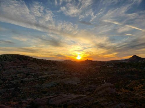 A vibrant sunset over rolling hills, with colorful clouds and a warm glow illuminating the landscape.