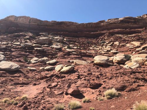 Rocky desert landscape with layered red rock formations and scattered boulders under a clear blue sky.