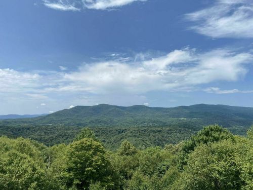 A panoramic view of lush green mountains under a blue sky with scattered clouds.
