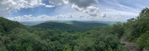 Panoramic view of lush green hills under a cloudy sky, showcasing a serene natural landscape.