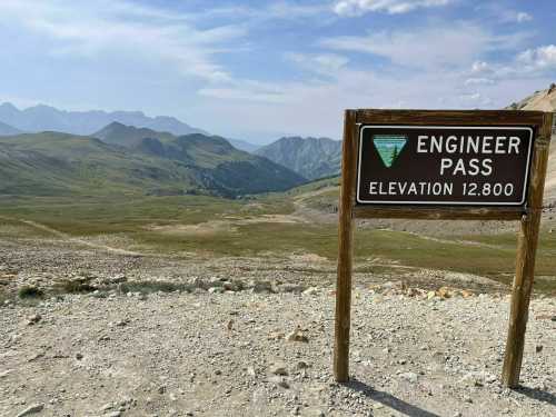 Sign for Engineer Pass at an elevation of 12,800 feet, with a scenic mountain landscape in the background.