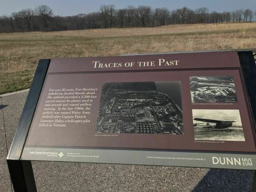 Sign titled "Traces of the Past" with historical information and aerial photos, set against a grassy landscape.