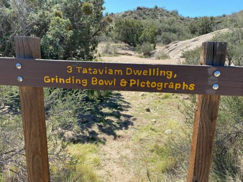 Signpost indicating the location of Tataviam dwelling, grinding bowl, and pictographs in a natural landscape.